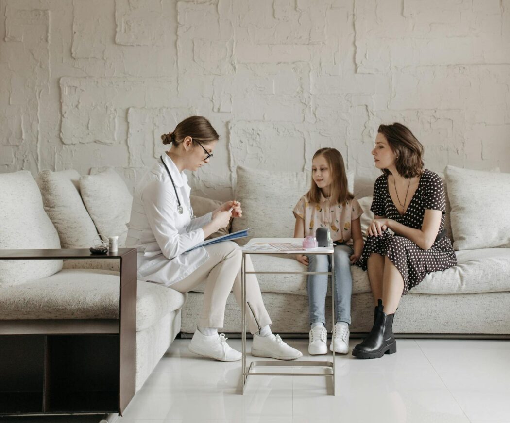 A doctor consults with a mother and child in a living room setting, highlighting personalized healthcare.